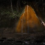 woman lays back on rock under waterfall