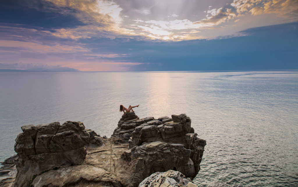 nude woman on cliff wearing only high heels looking towards Elba